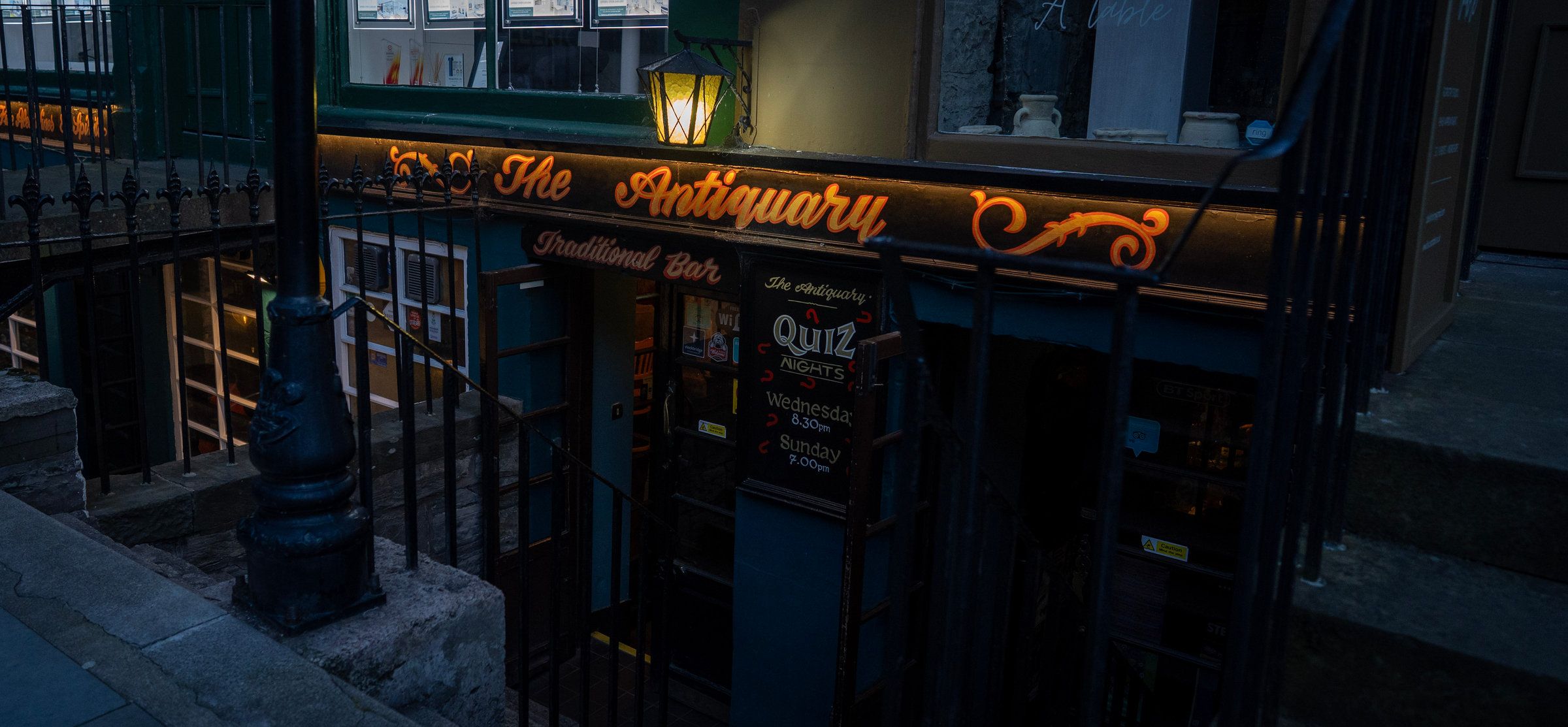 The Antiquary's lit frontage at dusk, the quiz board by the door and the steps down from St Stephen Street