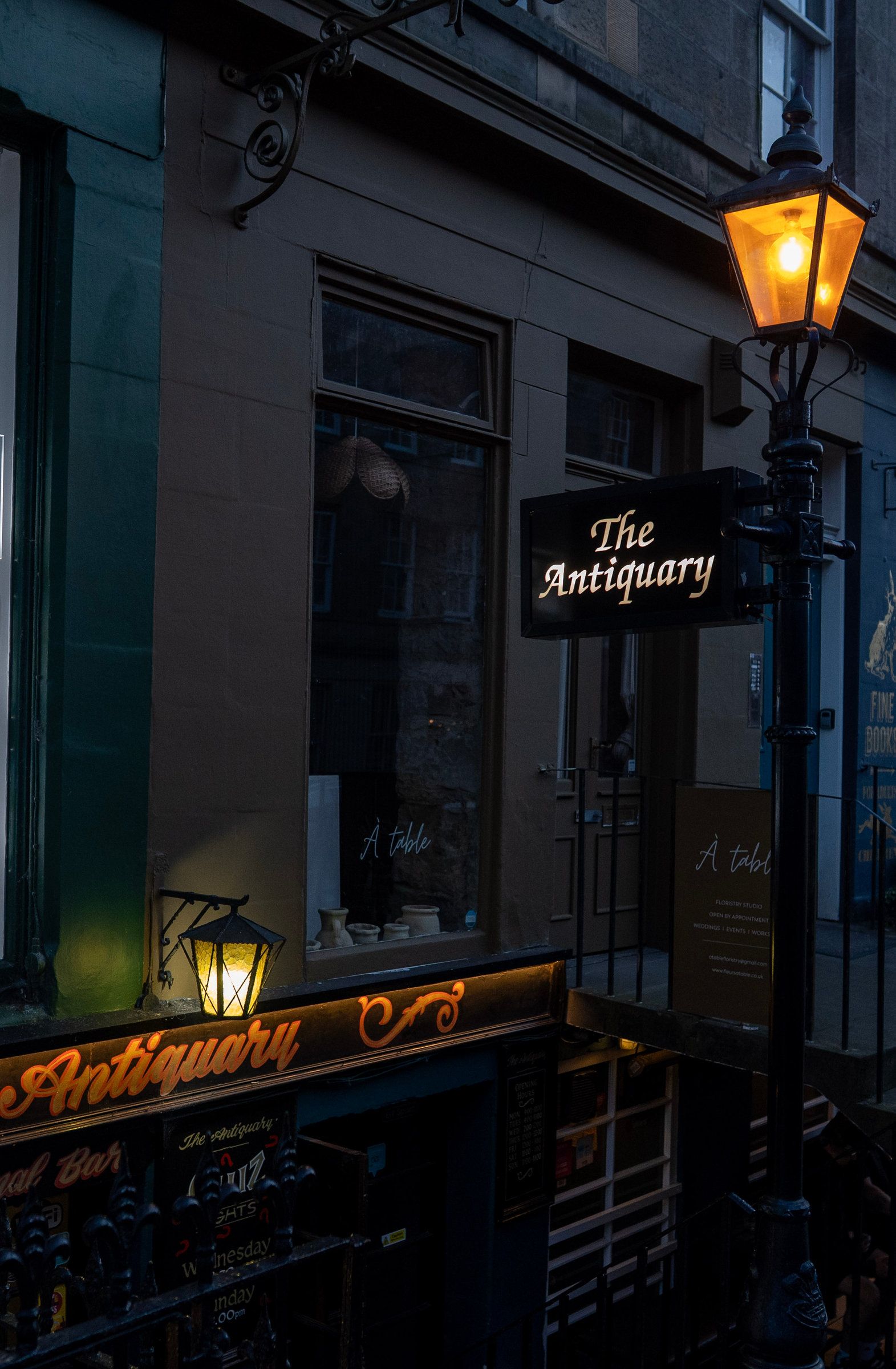 The lamp on St Stephen Street with The Antiquary's sign fixed to it, lit at dusk